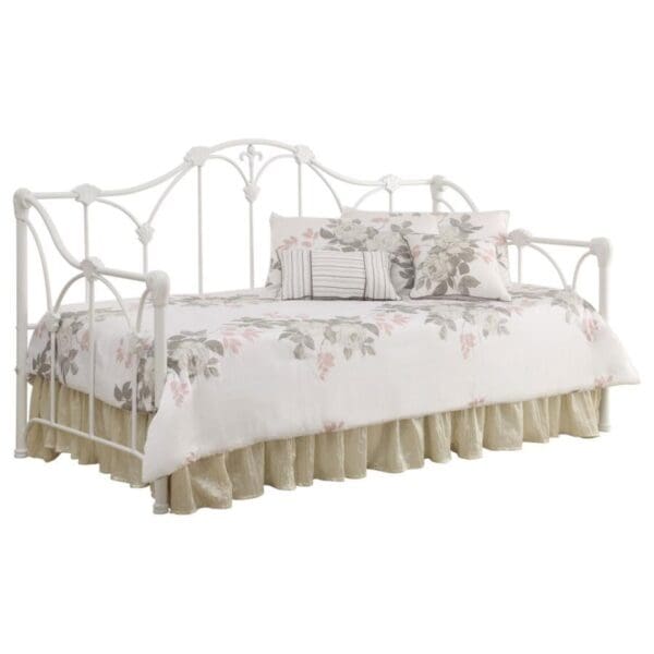 A white metal day bed with a beige and cream bedspread.