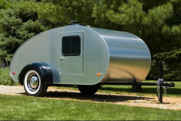 A small trailer parked on the grass near some trees.