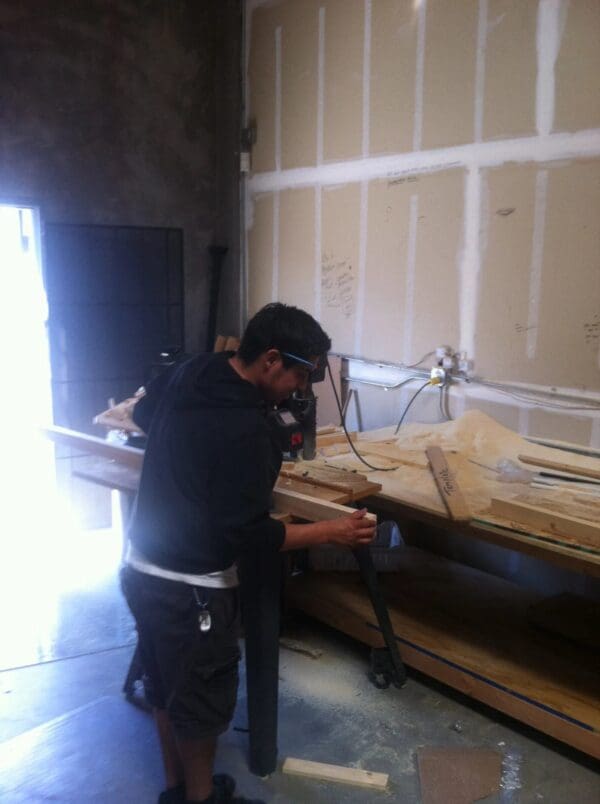 A man in black shirt holding drill near wooden table.