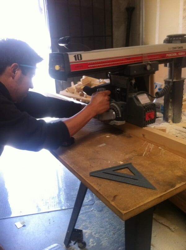 A man using a drill press on top of a wooden table.